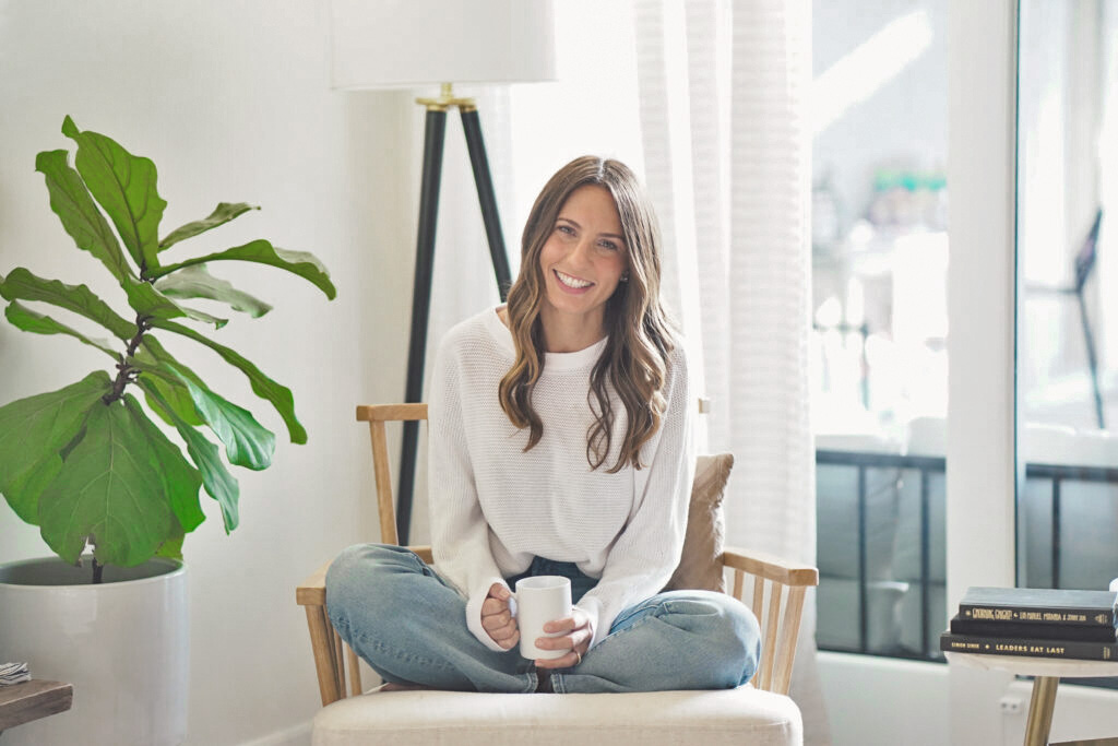 Erin Morrison, The Conscious Mom sitting in a chair, smiling and holding a cup of tea.